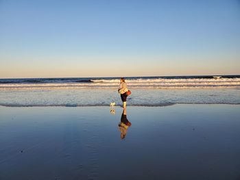Woman with dog standing on beach against clear sky