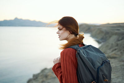 Side view of young woman looking at sea against sky