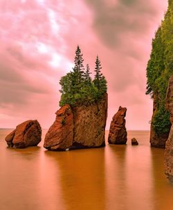 Rock formation in sea against sky during sunset