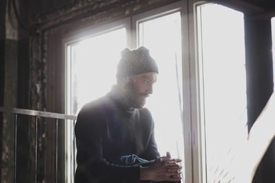 Young man looking through window at home