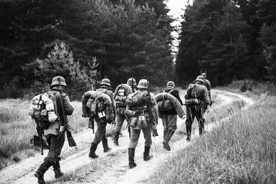 Rear view of army soldiers walking on field amidst trees in forest