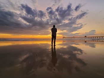 Silhouette man standing at beach against sky during sunset