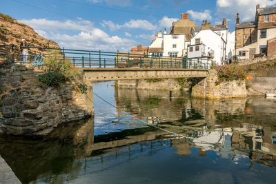 Bridge over river by buildings against sky