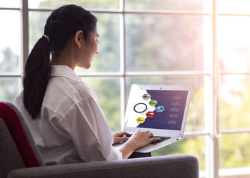 Woman using mobile phone while sitting on window