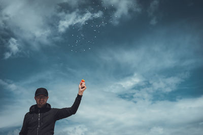 Portrait of young man firing confetti gun against sky