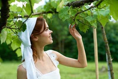 Side view of young woman standing against plants