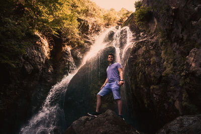 Full length of woman standing on rock at waterfall