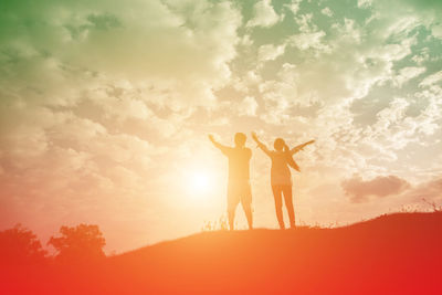 Friends standing on shore against sky during sunset