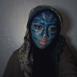 Portrait of young woman wearing mask against wall