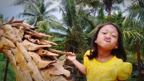 Portrait of girl holding plant against trees