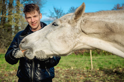 Portrait of young man feeding carrot to horse on field