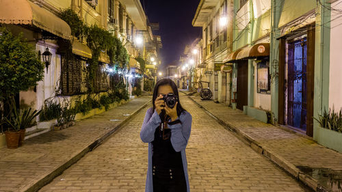 Woman standing on footpath amidst buildings in city at night