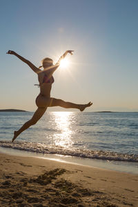 Woman in bikini jumping at beach against clear blue sky