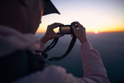 Man using mobile phone for photographing sunset point against sky