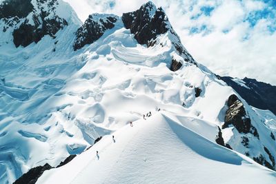 People hiking on snowcapped mountain against sky