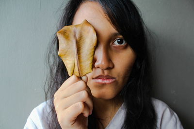 Close-up portrait of young woman holding dry leaf