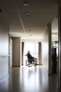 Side view of senior male patient sitting in wheelchair at hospital corridor