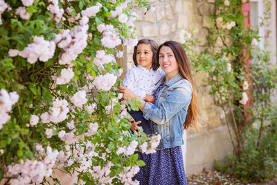 Mother and little handsome baby boy looking at bush with white roses