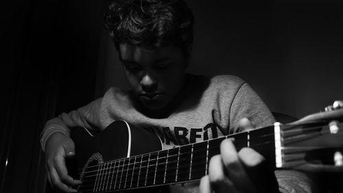 Young man playing guitar while sitting in darkroom