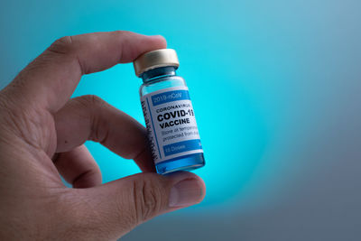 Close-up of hand holding bottle against blue background