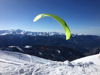 Person paragliding over snowy field against sky