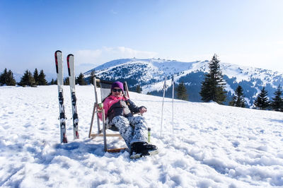 Young woman resting and drinking tea from a thermos after skiing on the ski slope on a sunny day. 