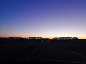 Road in city against clear sky at sunset