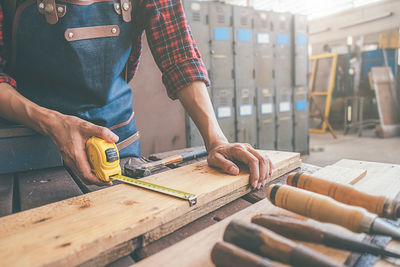 Midsection of carpenter measuring plank at workshop