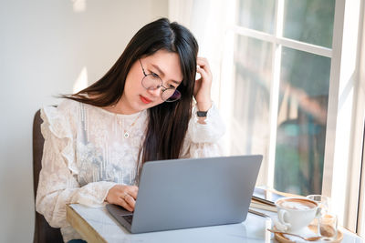 Young woman using phone while sitting on laptop