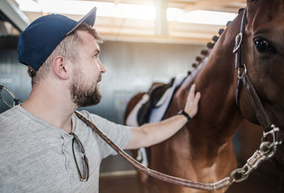 Man wearing cap touching horse