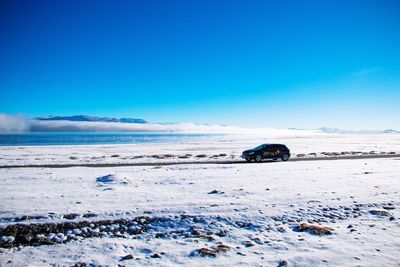 Cars on snow covered land against clear blue sky