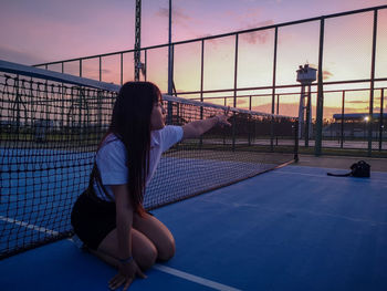 Woman sitting on court against sky during sunset