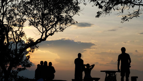 Silhouette people standing by tree against sky during sunset