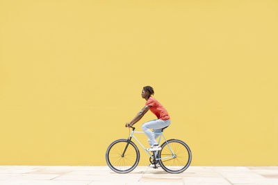 Black guy riding bicycle near wall