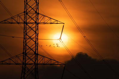 Low angle view of silhouette electricity pylon against sky during sunset