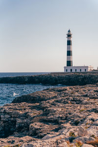 Lighthouse by sea against clear sky