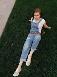 High angle view of young woman looking away while lying on grassy field