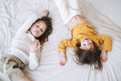 Cute little sisters girls on having fun on bed at home, top view