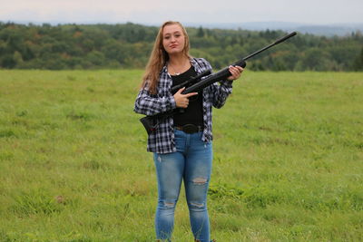 Portrait of teenage girl holding rifle while standing on field