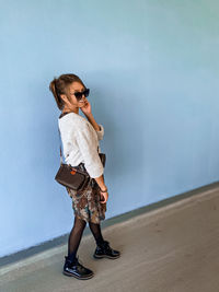 Young woman wearing sunglasses standing against wall