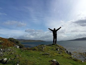 Man standing on rock by sea against sky