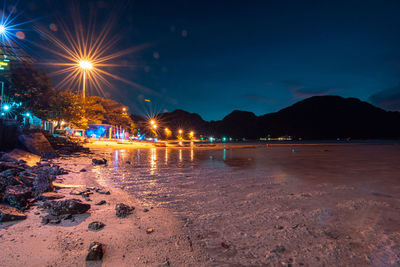 Illuminated city by sea against sky at night