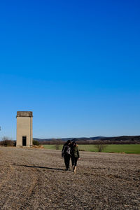 Rear view of people walking on field against clear sky