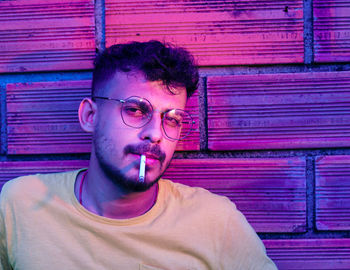 Portrait of young man smoking against wall