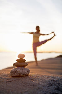 Woman practices yoga on lakeshore with focus on pile of stones