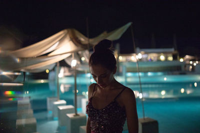 Rear view of woman standing against illuminated city at night