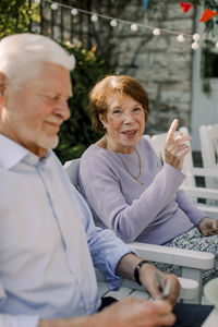 Portrait of smiling senior woman gesturing while sitting by man at back yard