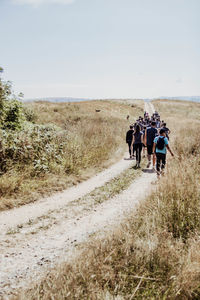 Rear view of people walking on field against sky