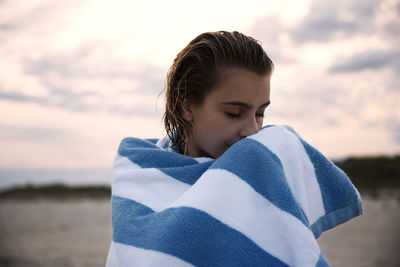 Woman with eyes closed wrapped in towel standing against sky