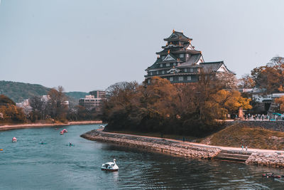 Boat in river by building against clear sky